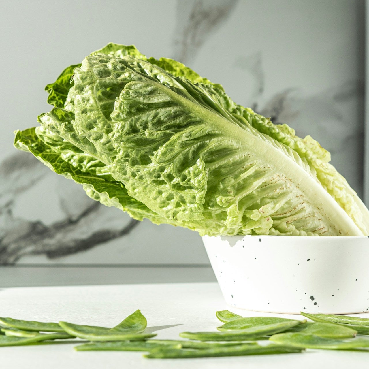 Green leafy lettuce in a white bowl on a marble countertop