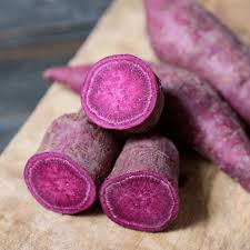 Three purple-skinned potatoes on a wooden surface with a blurred background