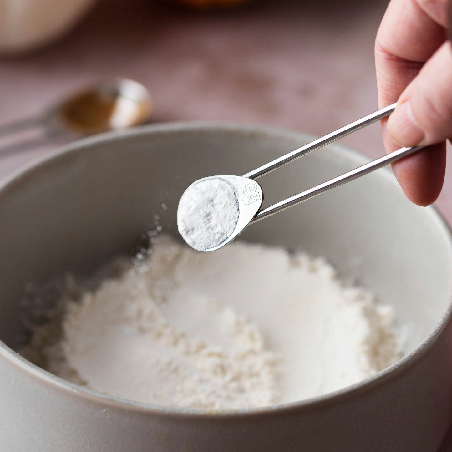 Hand using tongs to add salt to a bowl of flour with pumpkins in the background