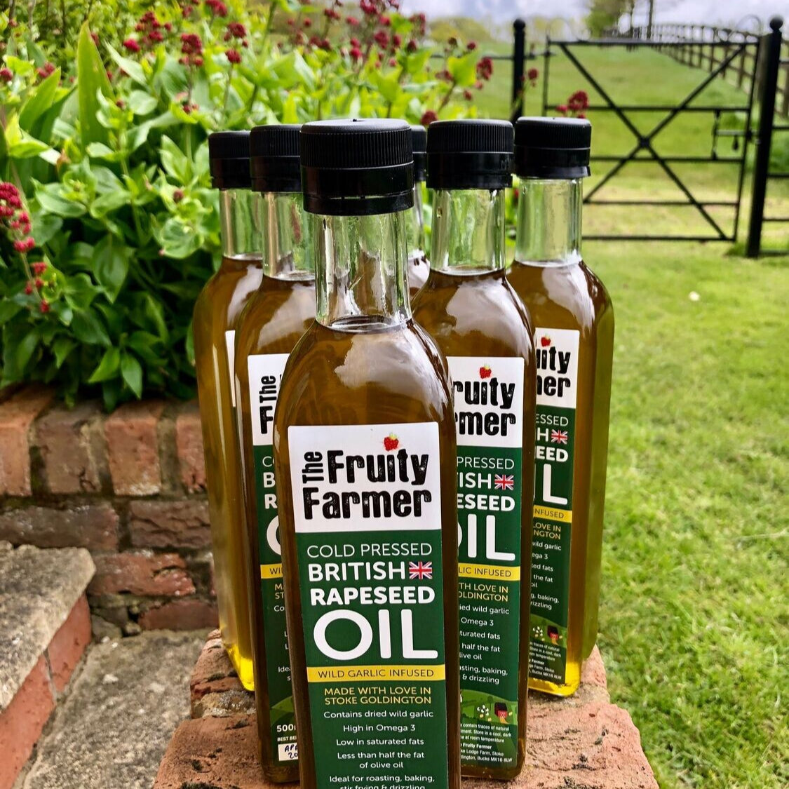 Bottles of 'The Fruity Farmer' oil on a brick ledge with a garden background