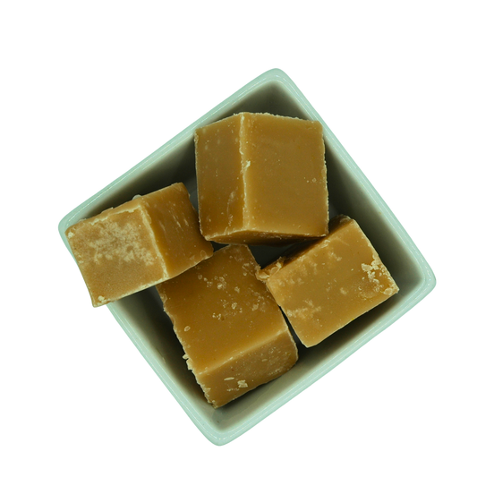 Cubes of caramel fudge in a white bowl on a white background