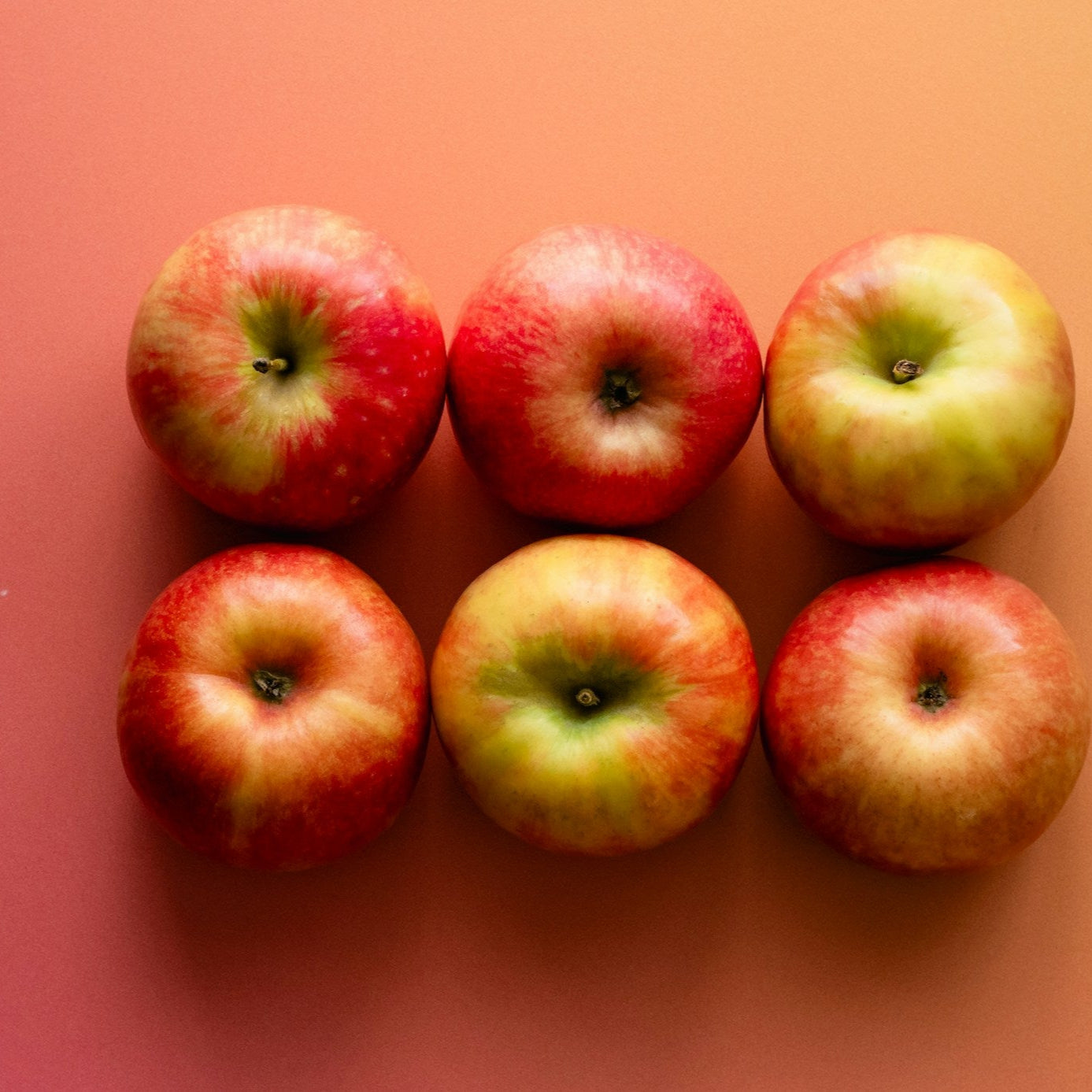 Six apples arranged in a row on a pink background