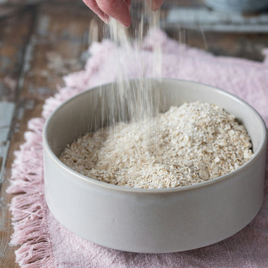Hand pouring oats into a bowl on a wooden surface