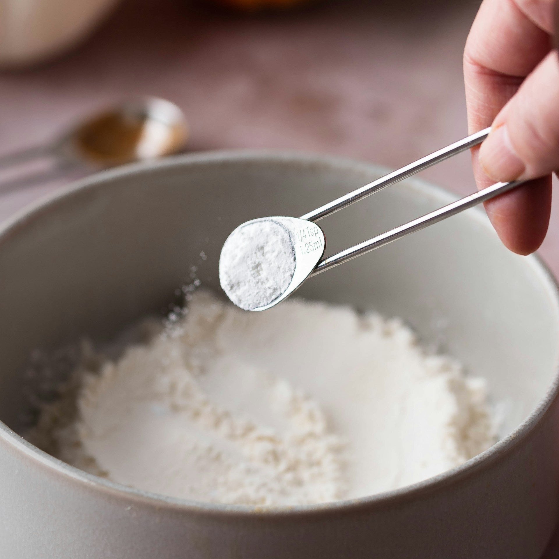 Hand using tongs to add salt to a bowl of flour with pumpkins in the background