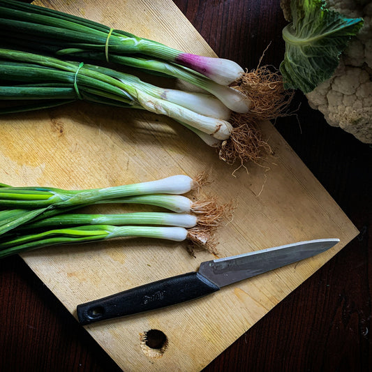Bundles of green onions on a wooden cutting board with a knife, next to a head of cauliflower.